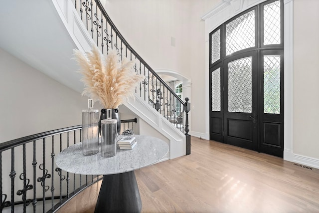 entrance foyer with baseboards, arched walkways, visible vents, wood finished floors, and a high ceiling