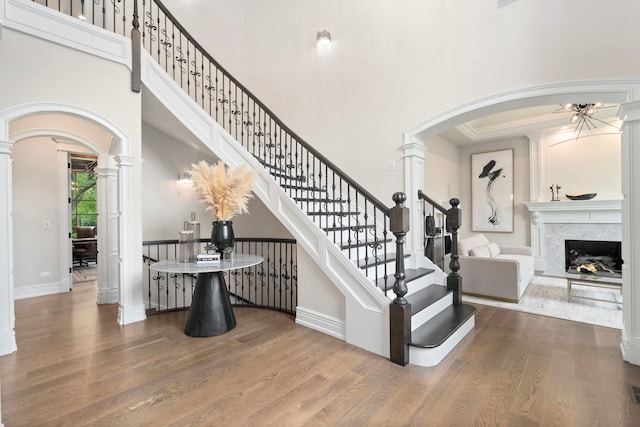 staircase featuring arched walkways, decorative columns, a high ceiling, and wood finished floors