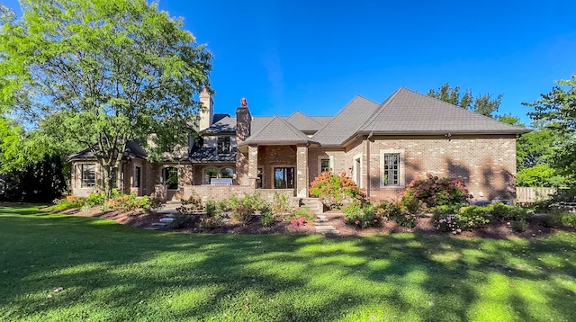 view of front facade featuring brick siding, a chimney, and a front yard