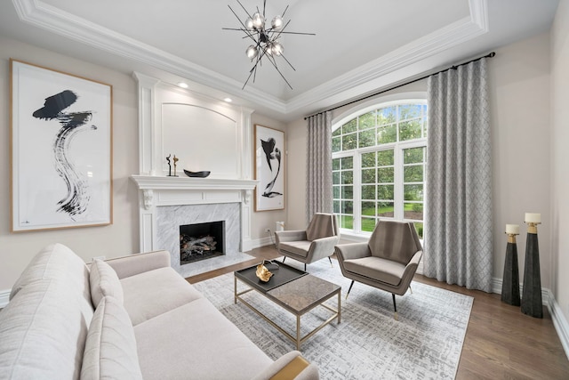 living room with a premium fireplace, ornamental molding, a raised ceiling, and wood finished floors