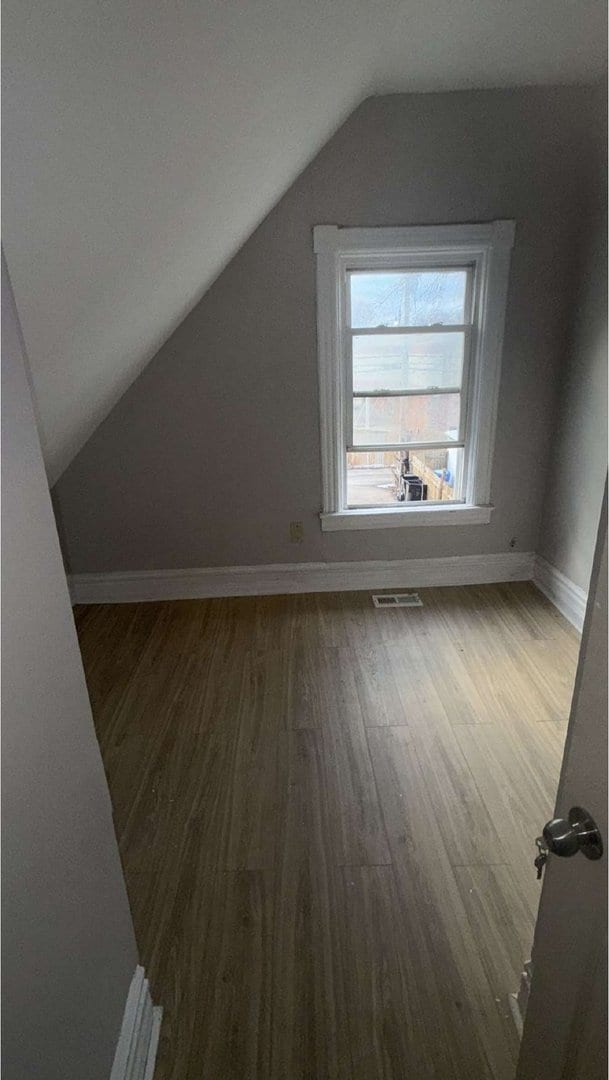 additional living space featuring vaulted ceiling, wood finished floors, visible vents, and baseboards