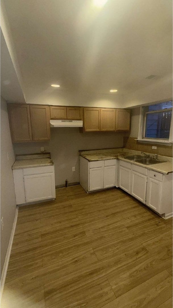 kitchen featuring white cabinetry, a sink, wood finished floors, under cabinet range hood, and baseboards