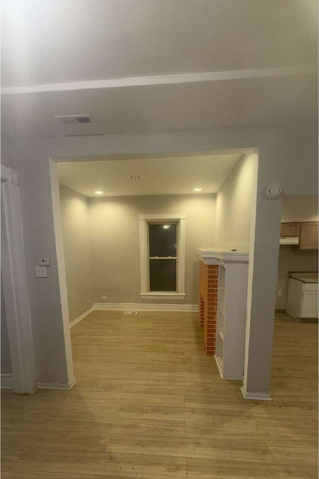 hallway with baseboards, visible vents, and light wood finished floors