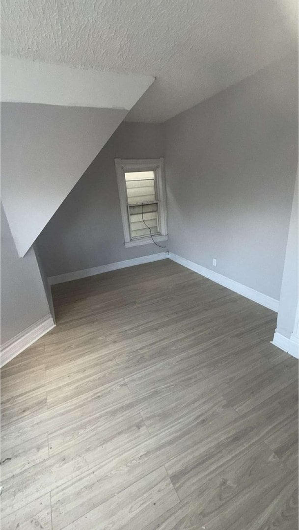 bonus room with a textured ceiling, vaulted ceiling, wood finished floors, and baseboards