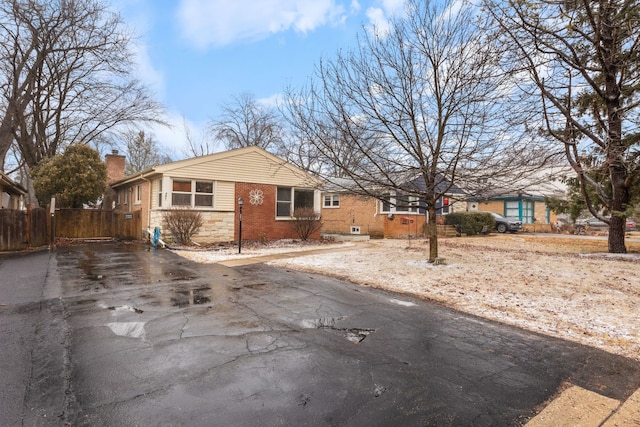 view of front of house with aphalt driveway, brick siding, fence, and a chimney