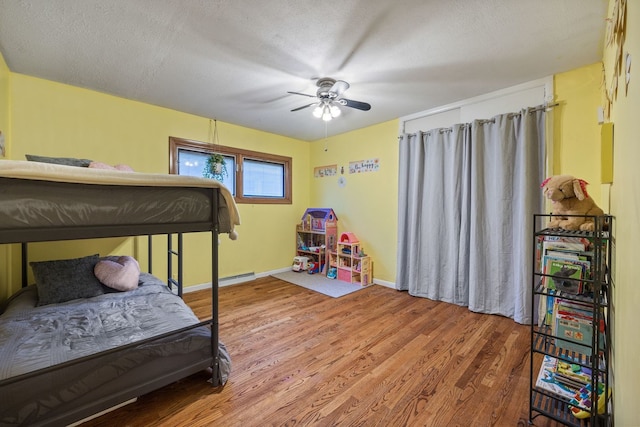 bedroom featuring a ceiling fan, a textured ceiling, baseboards, and wood finished floors