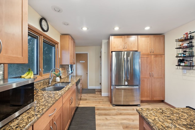 kitchen featuring stone counters, a sink, light wood-style floors, appliances with stainless steel finishes, and backsplash