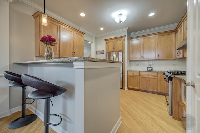 kitchen featuring under cabinet range hood, appliances with stainless steel finishes, decorative backsplash, a kitchen bar, and crown molding