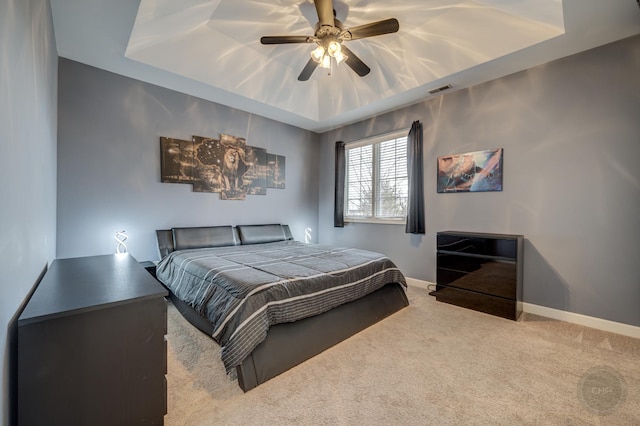 carpeted bedroom featuring a ceiling fan, a tray ceiling, visible vents, and baseboards