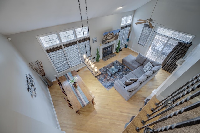 living area featuring high vaulted ceiling, baseboards, a fireplace with flush hearth, and wood finished floors