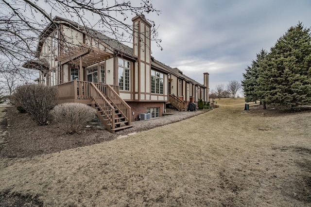 rear view of property with stairs, a yard, a chimney, and central air condition unit