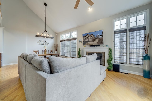 living area with high vaulted ceiling, a glass covered fireplace, wood finished floors, and baseboards