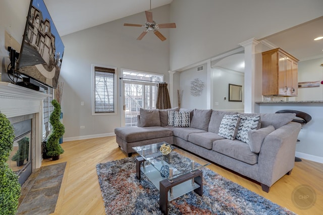 living area with baseboards, a tile fireplace, ceiling fan, ornamental molding, and wood finished floors