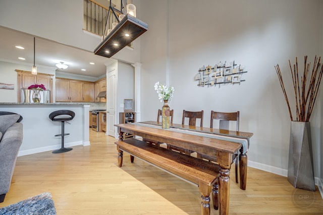 dining space featuring decorative columns, baseboards, ornamental molding, a high ceiling, and light wood-style floors