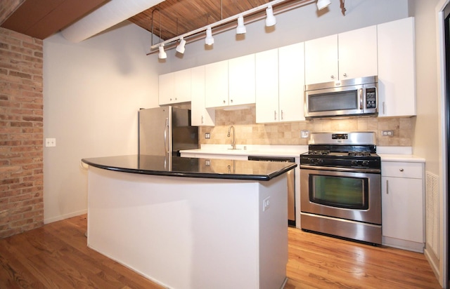 kitchen featuring a kitchen island, stainless steel appliances, white cabinets, light wood finished floors, and decorative backsplash