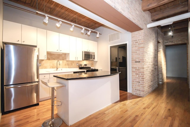 kitchen featuring light wood finished floors, brick wall, white cabinetry, and stainless steel appliances