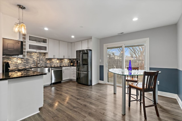 kitchen featuring refrigerator with ice dispenser, dishwasher, tasteful backsplash, dark countertops, and dark wood finished floors