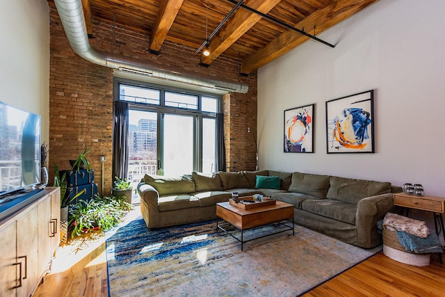 living room with a towering ceiling, brick wall, and wood finished floors