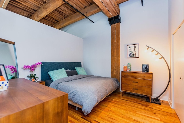 bedroom featuring baseboards, a towering ceiling, wood ceiling, beamed ceiling, and light wood-style floors