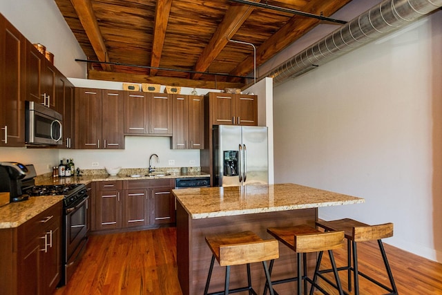 kitchen featuring a kitchen bar, appliances with stainless steel finishes, dark wood finished floors, and a sink