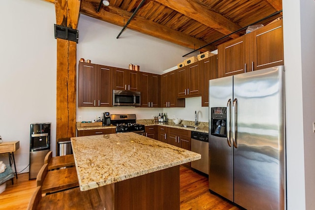 kitchen featuring wood finished floors, a sink, light stone countertops, stainless steel appliances, and beam ceiling