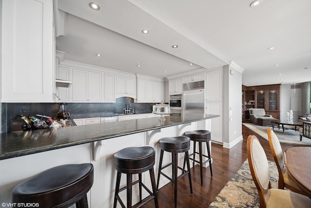 kitchen with dark wood-style flooring, stainless steel appliances, decorative backsplash, white cabinetry, and a peninsula