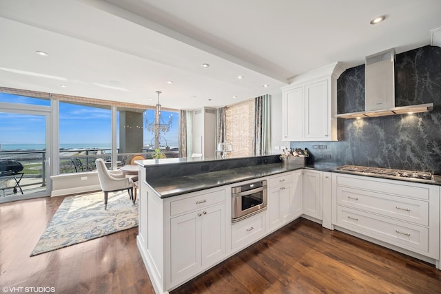 kitchen featuring appliances with stainless steel finishes, dark countertops, wall chimney range hood, and a peninsula