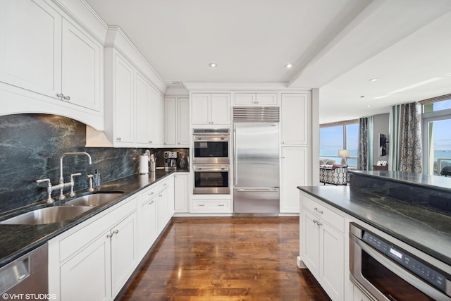 kitchen featuring dark wood-style floors, backsplash, appliances with stainless steel finishes, white cabinets, and a sink