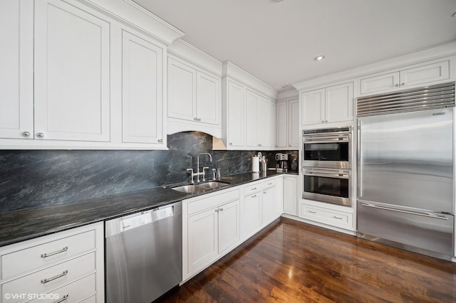 kitchen featuring white cabinets, decorative backsplash, appliances with stainless steel finishes, dark wood-type flooring, and a sink