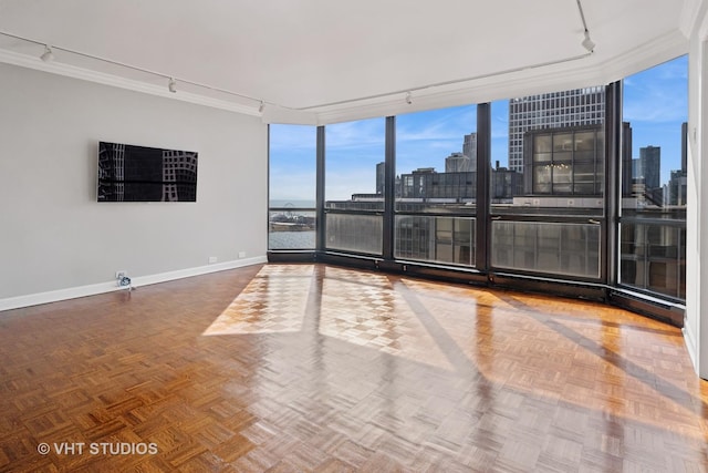 unfurnished room with a city view, ornamental molding, floor to ceiling windows, rail lighting, and baseboards