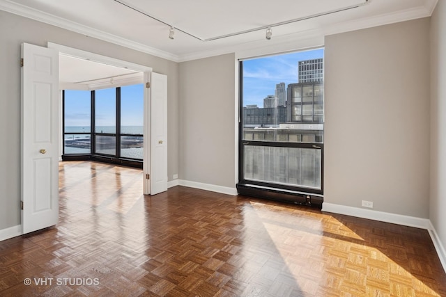 spare room featuring rail lighting, a view of city, baseboards, and ornamental molding