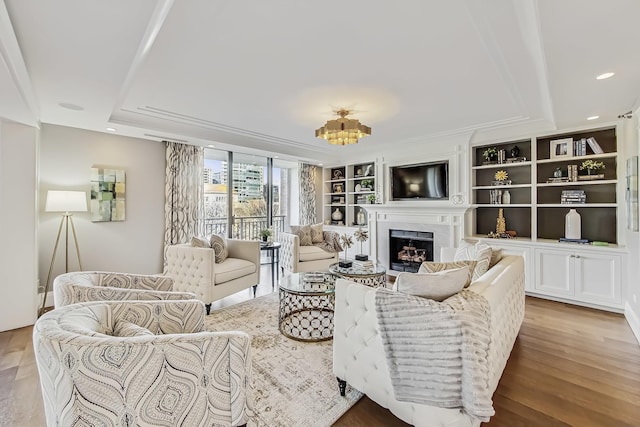 living area with built in features, wood finished floors, recessed lighting, a fireplace, and a raised ceiling