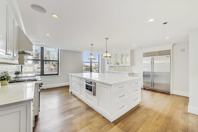 kitchen with tasteful backsplash, light wood-type flooring, light countertops, white cabinets, and high end appliances