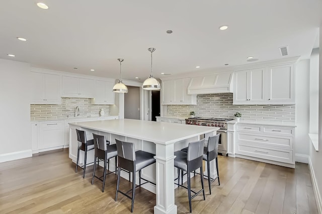 kitchen with a spacious island, custom exhaust hood, stainless steel stove, light countertops, and white cabinetry