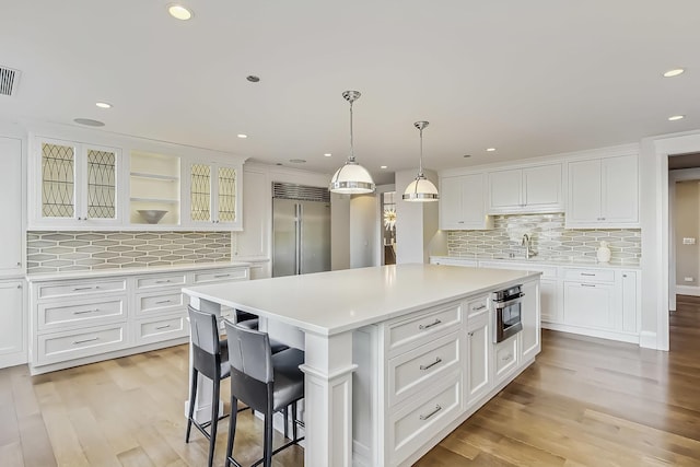 kitchen featuring light wood-style flooring, stainless steel appliances, light countertops, glass insert cabinets, and white cabinetry