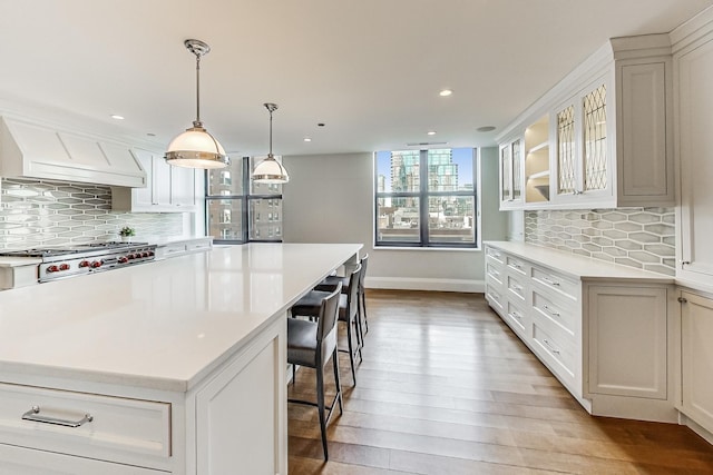 kitchen with custom range hood, a center island, stainless steel gas stovetop, light countertops, and glass insert cabinets