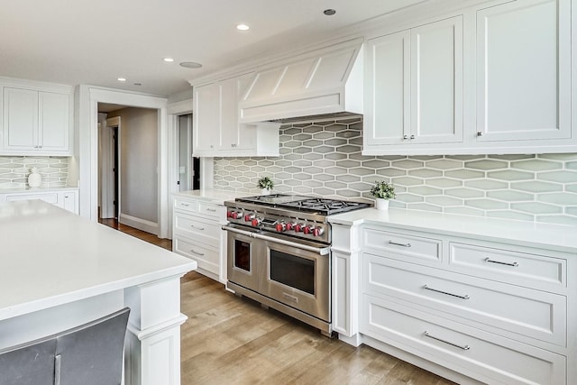 kitchen featuring range with two ovens, light countertops, custom range hood, white cabinets, and light wood-type flooring