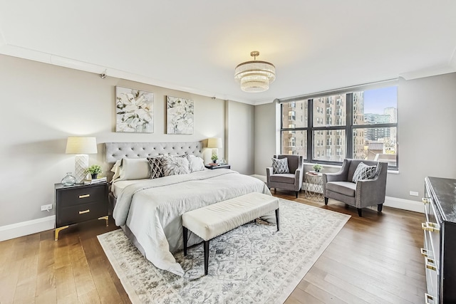 bedroom featuring a view of city, hardwood / wood-style floors, baseboards, and ornamental molding