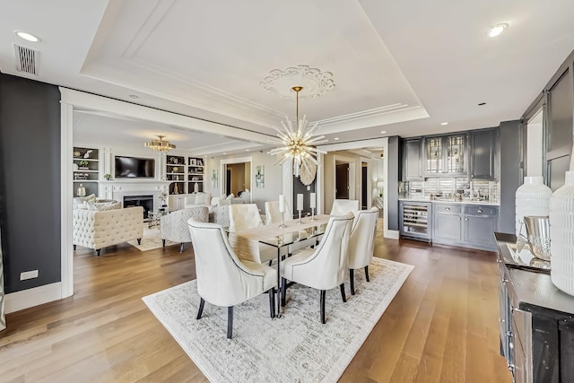 dining area featuring visible vents, a notable chandelier, beverage cooler, a tray ceiling, and a fireplace