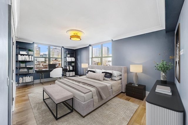 bedroom with a view of city, light wood-style flooring, baseboards, and ornamental molding