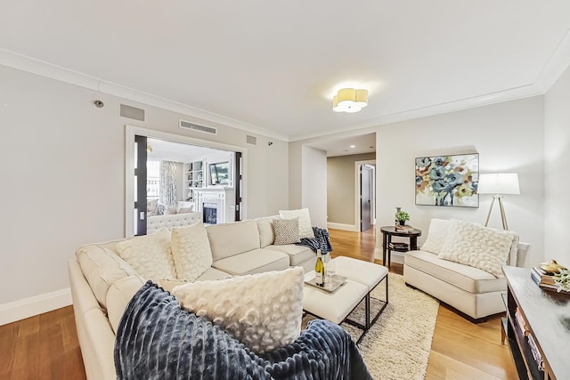 living room with light wood-style flooring, visible vents, and ornamental molding