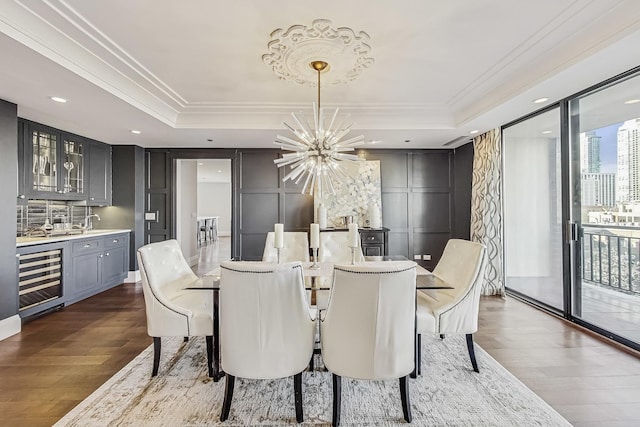 dining space with beverage cooler, ornamental molding, a tray ceiling, an inviting chandelier, and a decorative wall