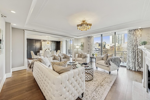 living area with hardwood / wood-style flooring, a tray ceiling, a high end fireplace, an inviting chandelier, and baseboards