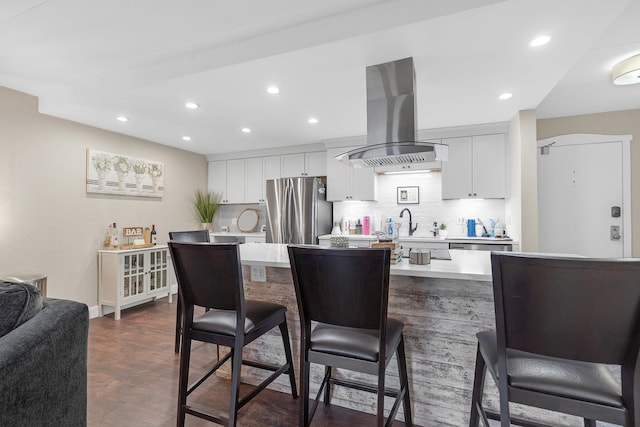 kitchen featuring island range hood, light countertops, a kitchen breakfast bar, and freestanding refrigerator