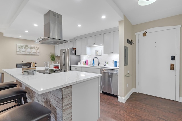 kitchen featuring island range hood, dark wood-type flooring, a kitchen island, appliances with stainless steel finishes, and a kitchen bar