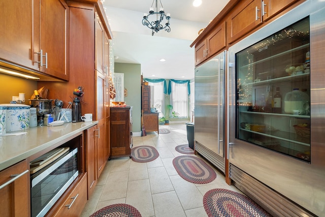 kitchen featuring built in fridge, stainless steel microwave, brown cabinets, light countertops, and light tile patterned flooring