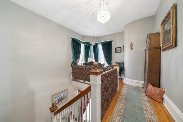 corridor with baseboards, wood finished floors, an upstairs landing, and a notable chandelier