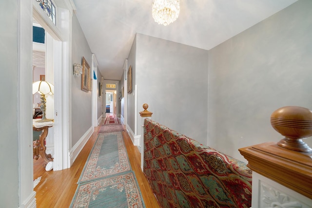 corridor with baseboards, a chandelier, and wood finished floors