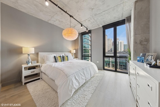 bedroom featuring access to exterior, floor to ceiling windows, a view of city, light wood finished floors, and rail lighting