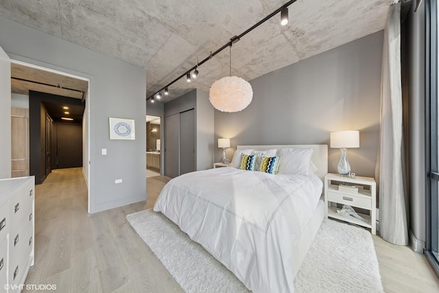 bedroom featuring baseboards, light wood finished floors, ensuite bath, and track lighting